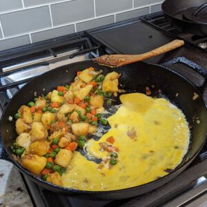 Adding scrambled eggs to the pan with vegetables in pineapple fried rice recipe