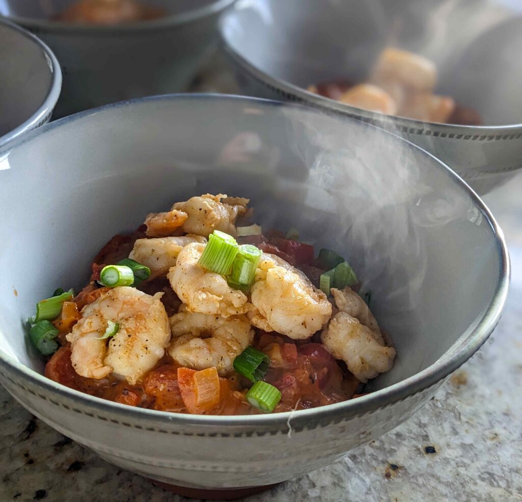 A bowl of the shrimp and grits recipe with steaming hot creamy grits and large succulent shrimp on top.