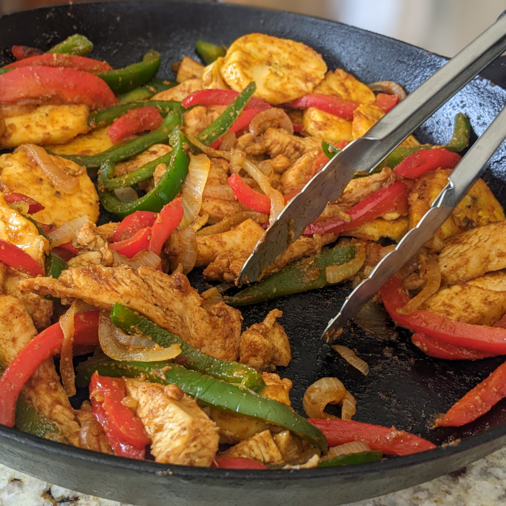 Chicken fajita with plantains in a cast iron skillet, served with tongs.