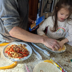 Parent helping child assemble Tilapia Fajita quesadilla recipe. Adding cheese to the bottom layer.  