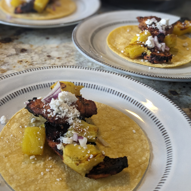 Three plates featuring delicious Tacos Al Pastor served on corn tortillas and topped with charred pineapple and cotija cheese.