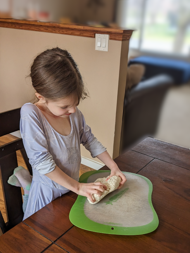 A little chef helping out in the kitchen kneading pizza dough.  
