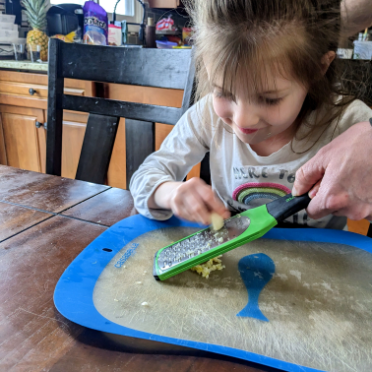 Little girl grating garlic with a micro grater for vegan tofu stir fry recipe.