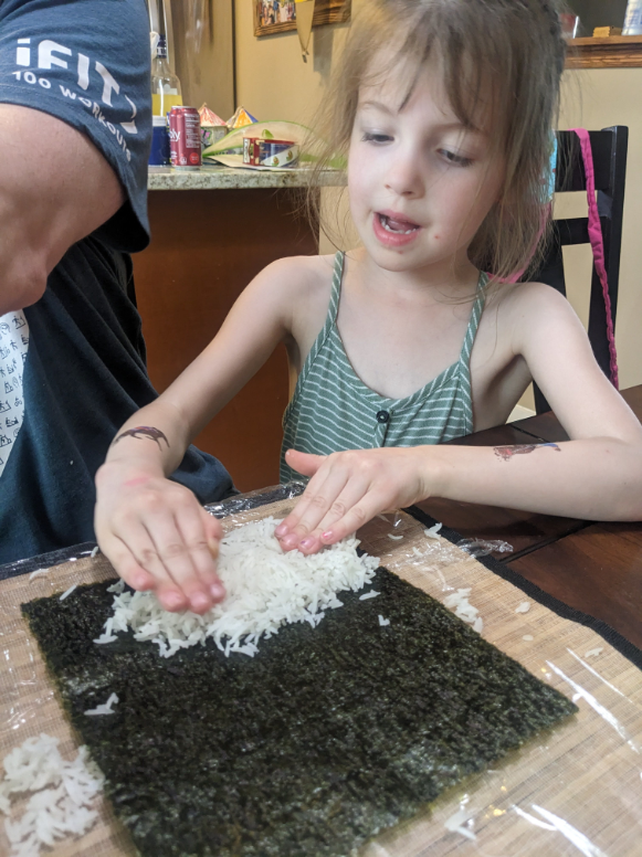 Assisting with spreading the sushi rice on the nori to start assembling the sushi rolls.