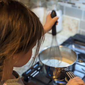 A little chef using a whisk to create a smooth bechamel suace.
